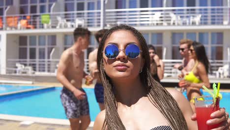 joven hermosa con dreads y gafas de sol acercándose a la cámara mientras baila en la fiesta de la piscina. feliz joven alegre