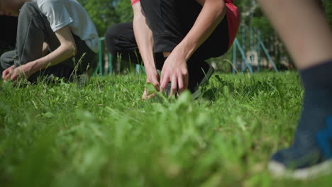 close-up view of three people s legs on a grassy field, focusing on two individuals squatting down as they adjust their shoes