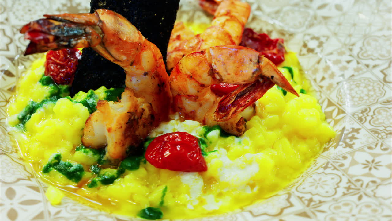 Close up of saffron risotto topped with grilled prawns and roasted cherry tomatoes