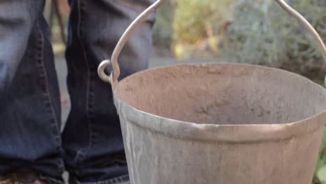 lady picking up metal bucket on garden pathway close up