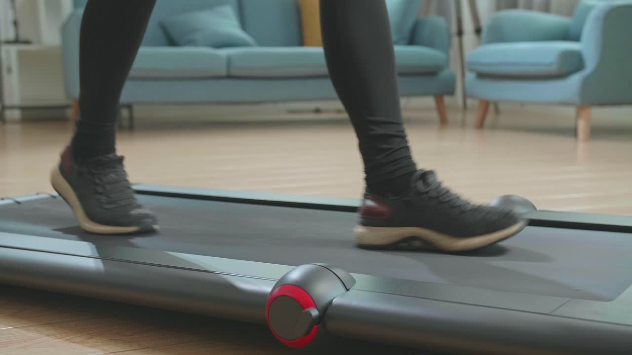 vista lateral de las piernas de una mujer asiática entrenando en una cinta de correr en casa