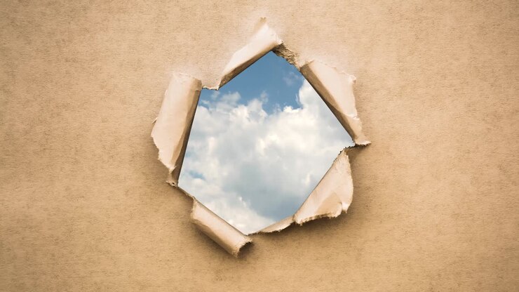 Creative 4k time laps video of fast moving clouds in the blue sky that are visible through a circle hole with torn edges in old retro grunge vintage paper.
