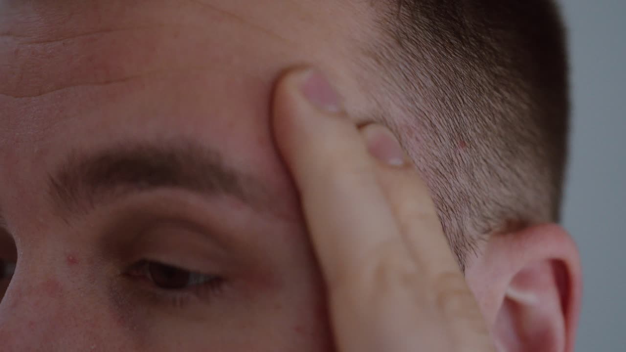 Primo piano di un uomo che si preme e massaggia la tempia, esprimendo tensione e disagio. Concetto di mal di testa, emicrania, stress, sovraccarico mentale e problemi di salute