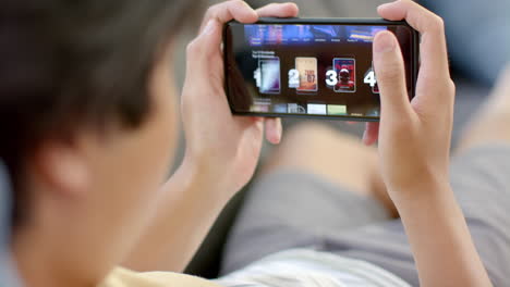 un adolescente asiático navega por un servicio de transmisión de video en un teléfono inteligente en casa