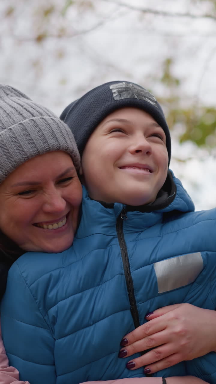 la madre tiene affettuosamente in braccio il figlio mentre sorridono durante una passeggiata d'autunno, con lui che tiene un bastone e interagisce giocosamente con la natura, creando un momento di legame familiare caldo e gioioso all'aperto