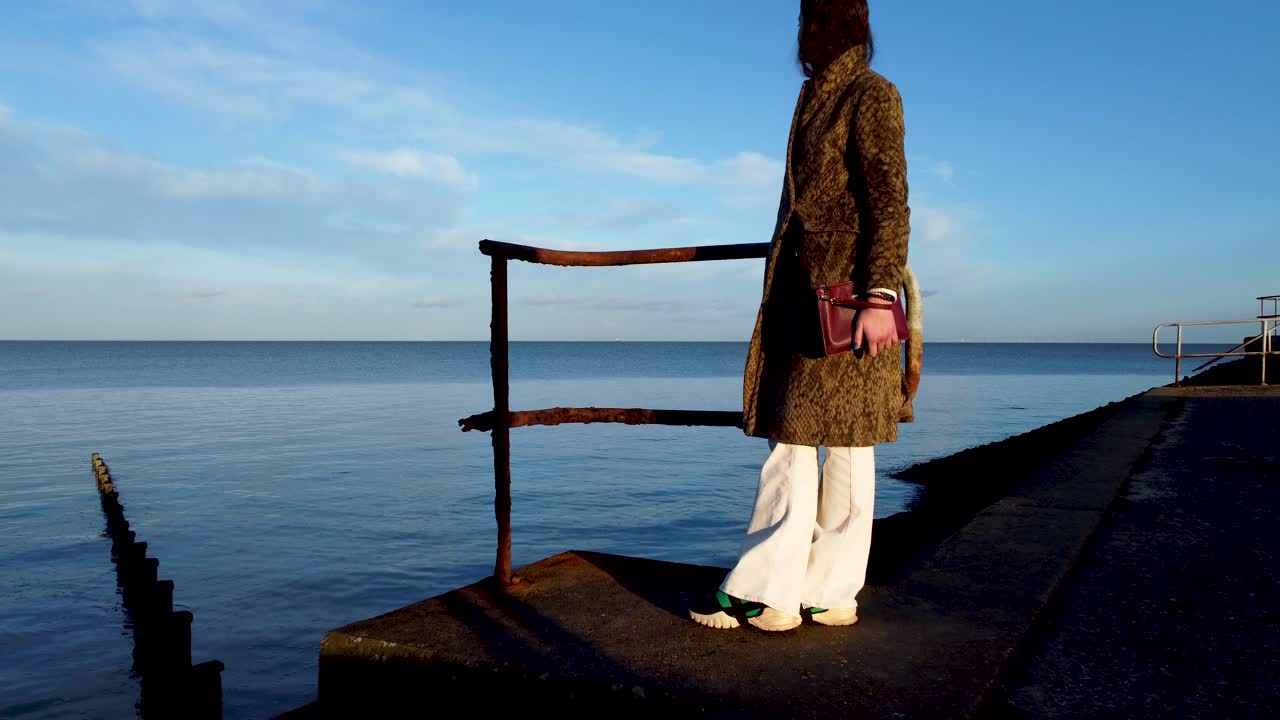 바다를 바라보고 있는 여성, 수평선까지 카메라는 부두 근처의 녹슨 부두를 통해 움직입니다.