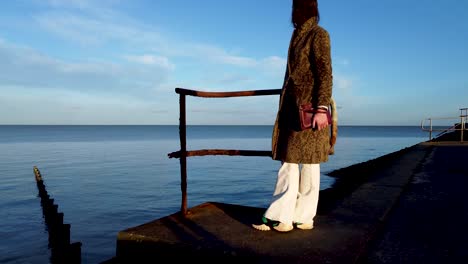 Mujer-Mirando-El-Mar,-Hasta-El-Horizonte,-La-Cámara-Se-Mueve-A-Través-De-Un-Muelle-Oxidado-Cerca-De-Un-Muelle