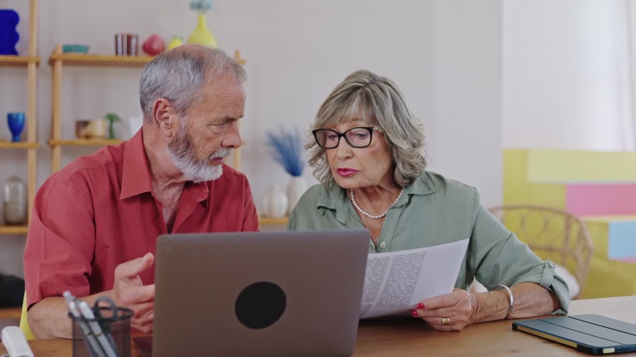 Casal de idosos olhando documentos e laptop em casa