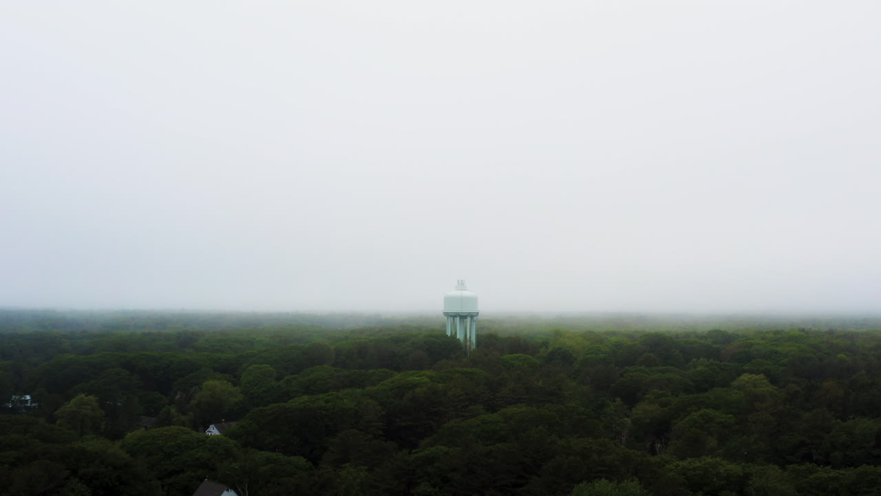 drone aerial of water tower above lush green trees in thick fog and foggy misty moody weather 4k 30p