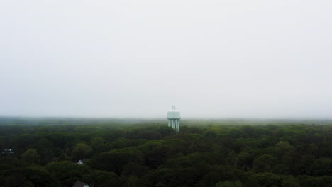drone aerial of water tower above lush green trees in thick fog and foggy misty moody weather 4k 30p