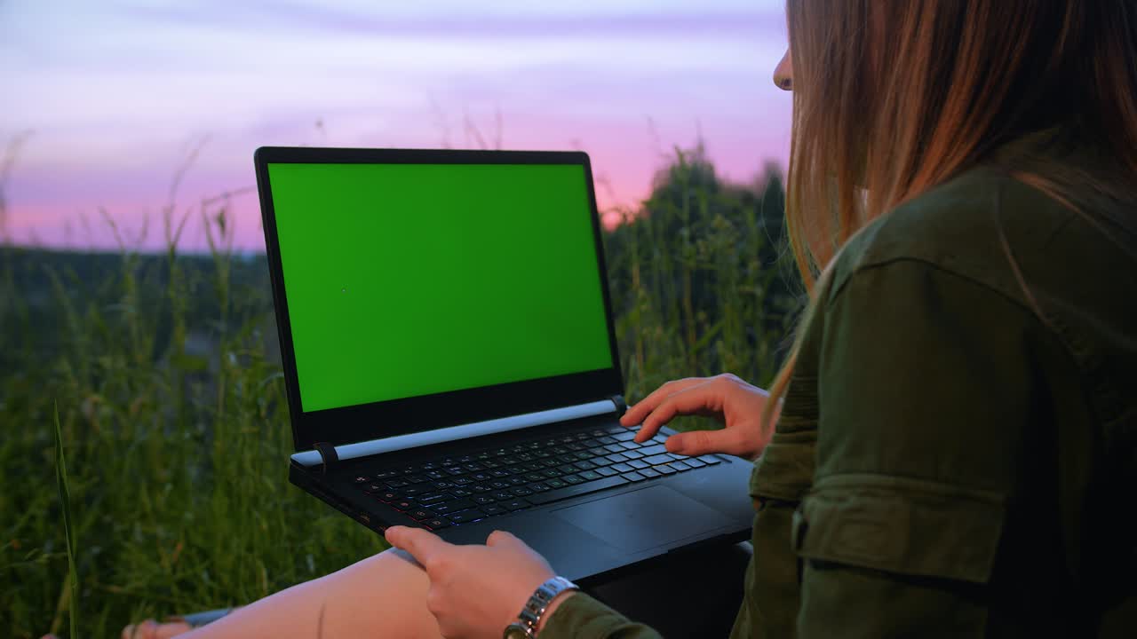 joven trabajando en una computadora portátil con una pantalla verde en la naturaleza en verano.