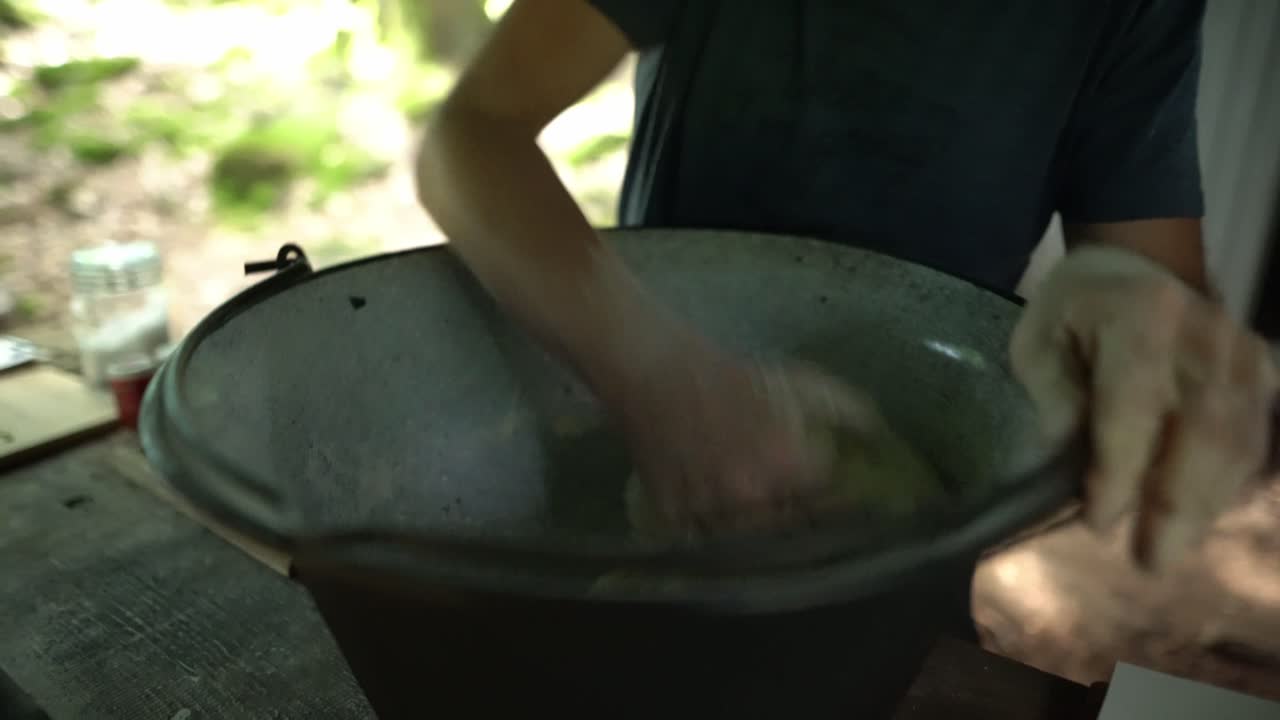 Uomo che impasta la pasta del pane in una grande ciotola di metallo in una cucina da campo all'aperto. Panificazione tradizionale, cucina bushcraft e preparazione di cibo da sopravvivenza in natura