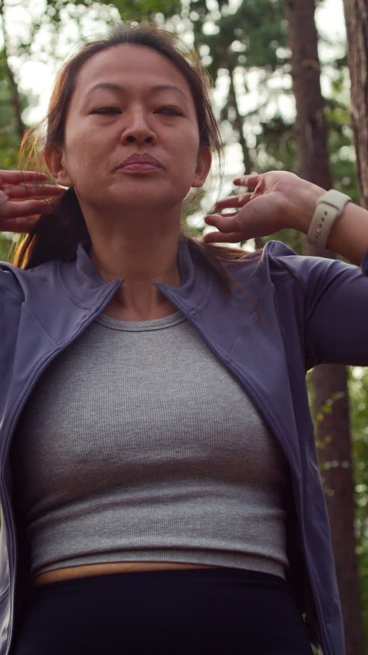 Video verticale di una donna che si allena all'aperto correndo lungo un sentiero nel bosco, fermandosi per riprendere fiato e controllando l'app di attività sullo smartwatch, ripreso in tempo reale