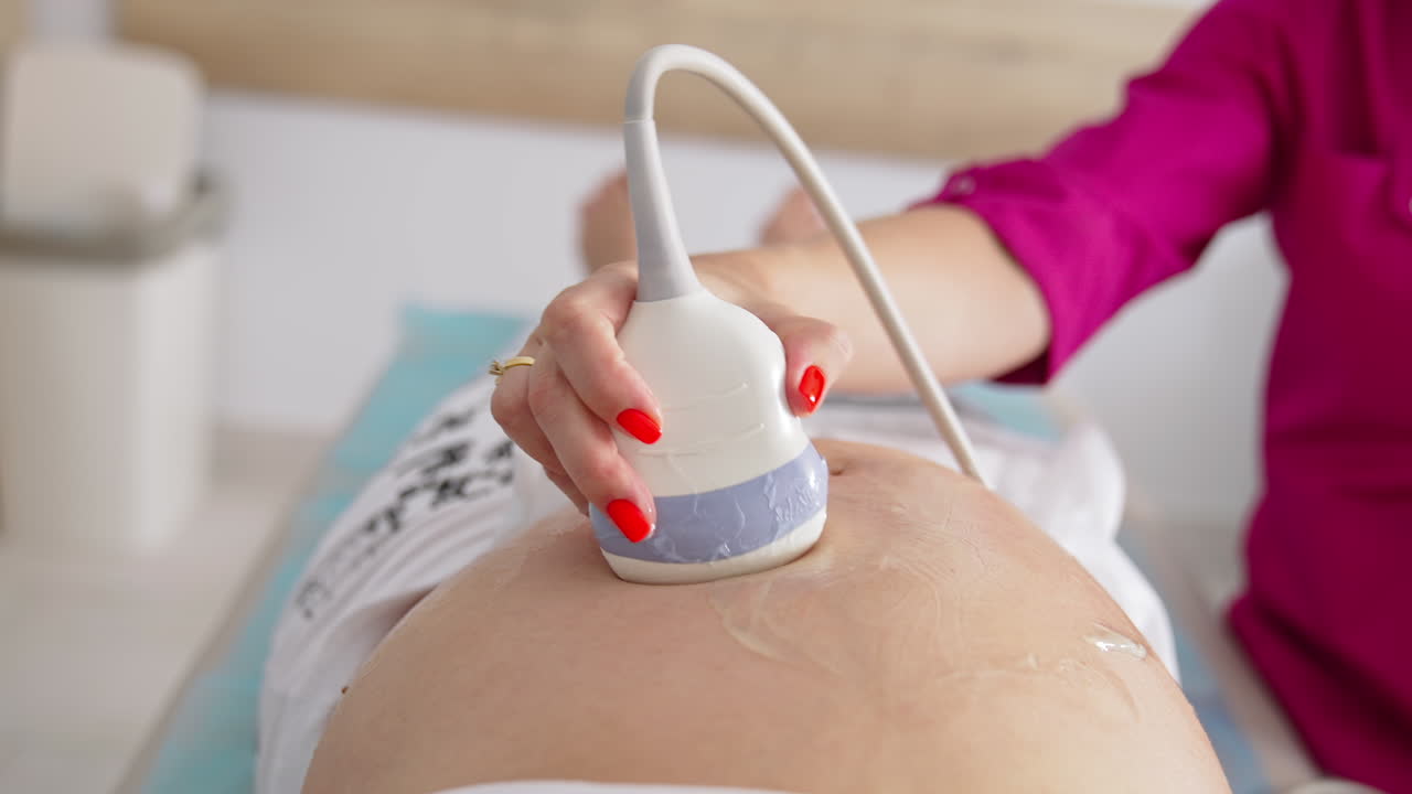 Ultrasound scan to a pregnant woman in hospital. Gynecologist using transducer on female's belly during sonography procedure.