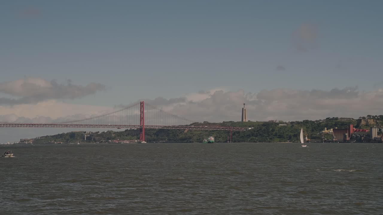 red suspension bridge and distant christ statue viewed from lisbon riverside