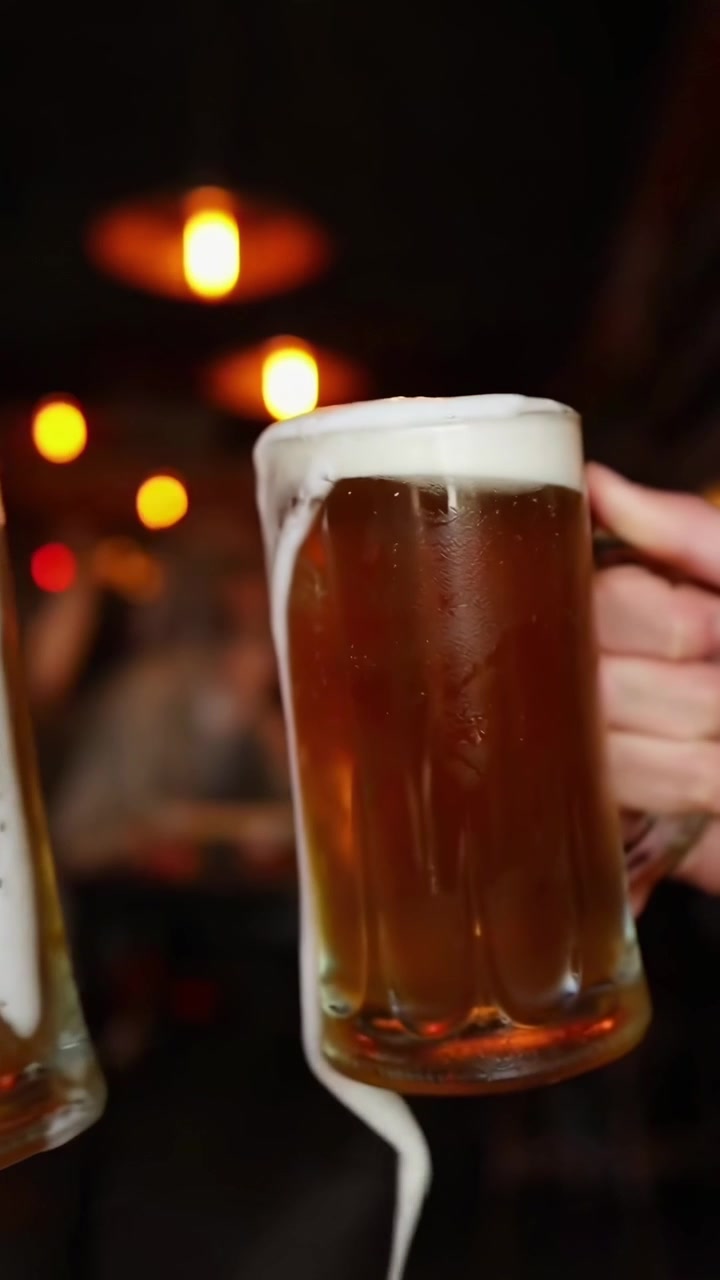 Due boccali di birra che si scontrano e traboccano di schiuma in un bar