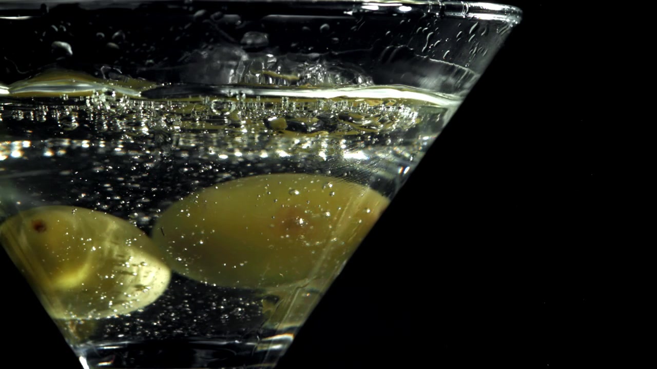 Olive verdi frizzanti in un calice da Martini su sfondo nero