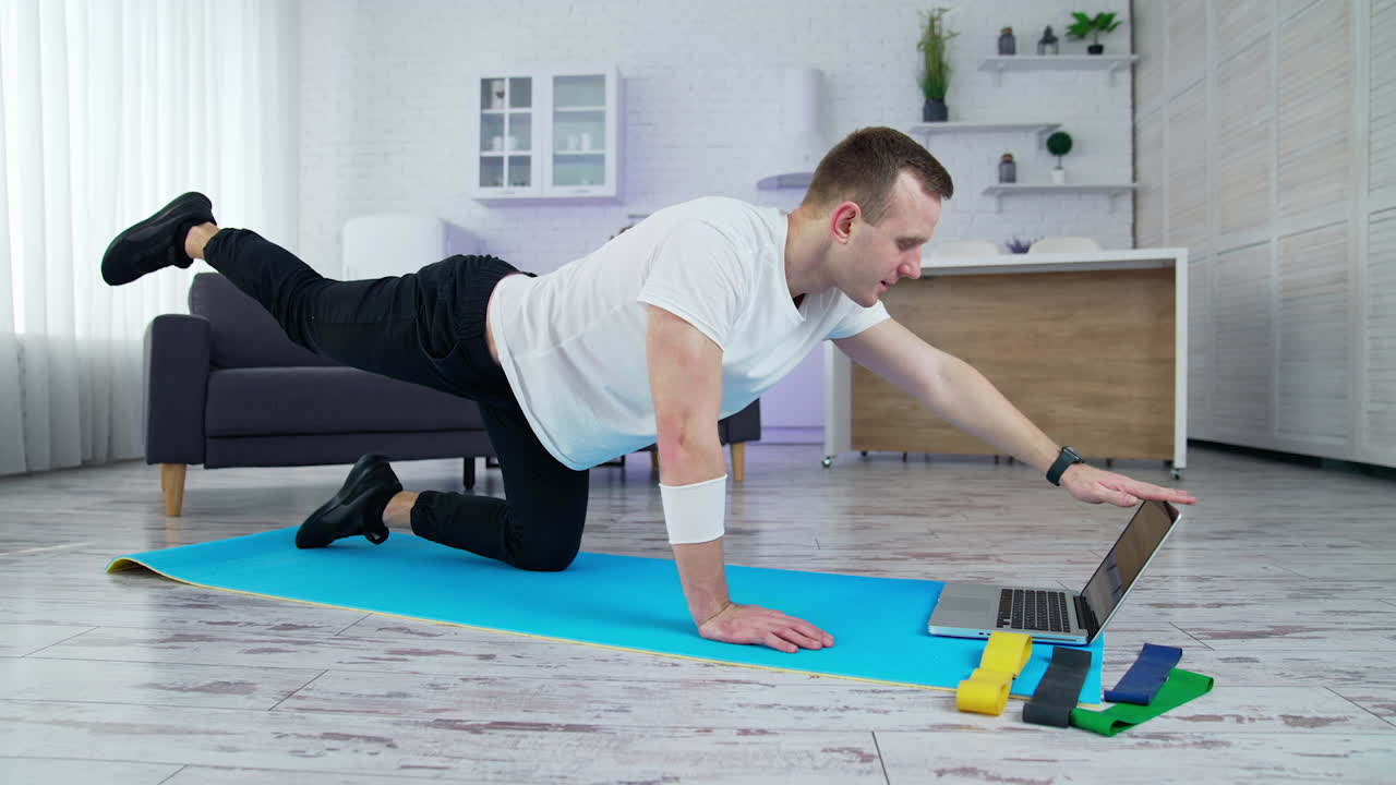 Young lifestyle sportsman working out in front of his laptop computer at home. Training body indoor by strong handsome man. Full length
