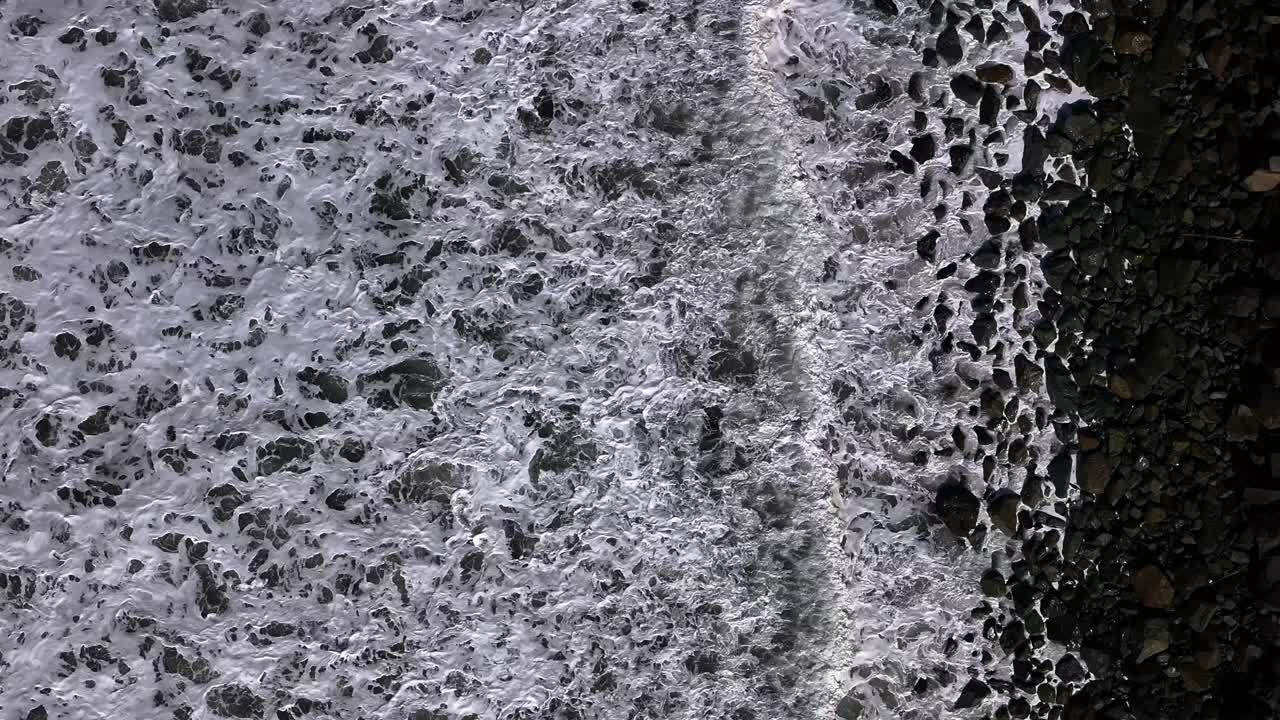 이 코 아래의 공중 촬영은 어두운 날 해변에 부히는 물결을 포착합니다.