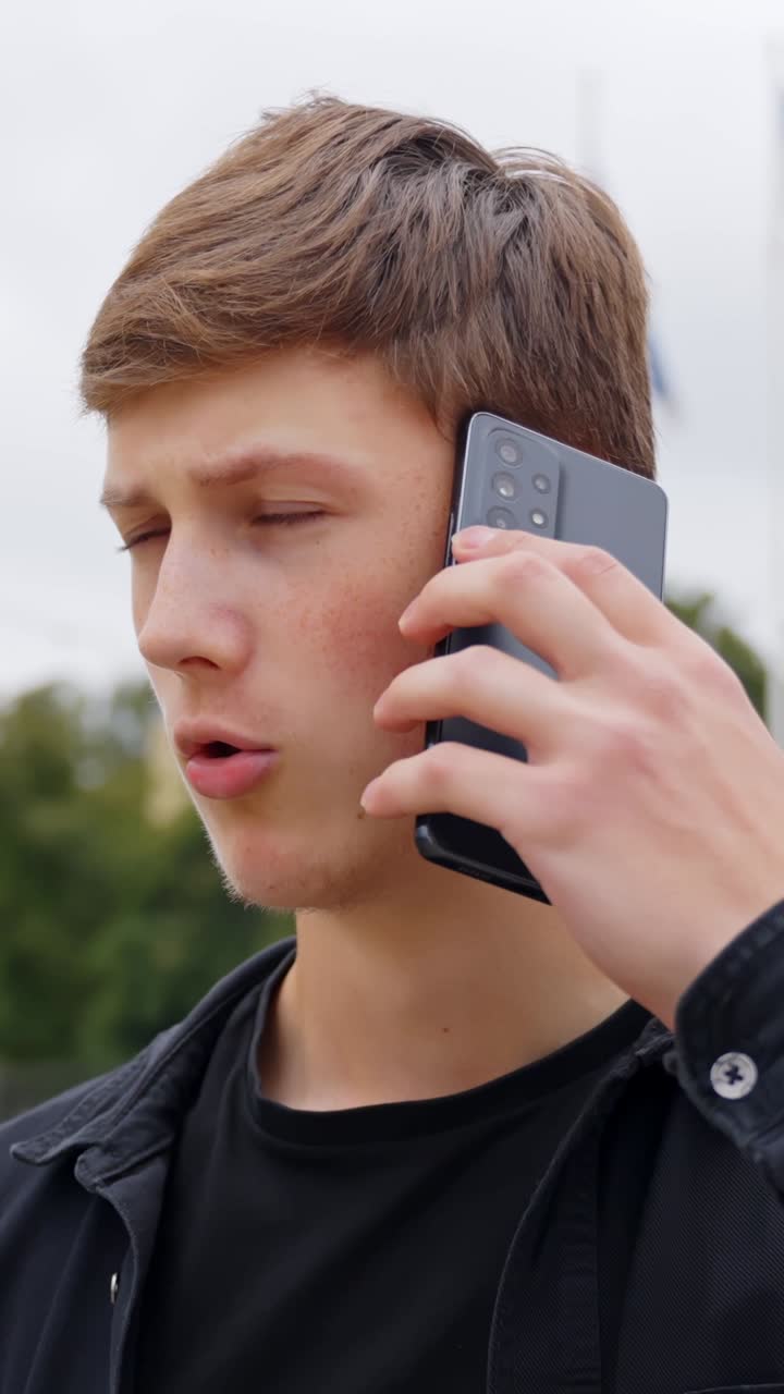Man answers phone while walking outdoors with confused expression and gestures with hands