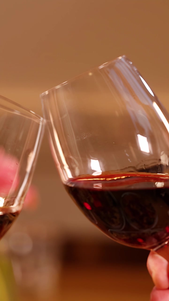 Mani che brindano con bicchieri di vino rosso durante una cena romantica con illuminazione calda e sfondo bokeh.