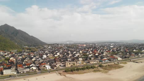panorámica aérea derecha sobre la ciudad costera japonesa con montañas en un día brillante