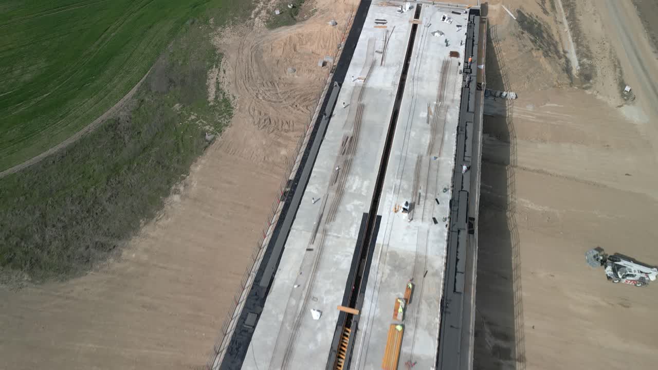 Overhead drone view of a bridge construction with workers, machinery, and materials scattered