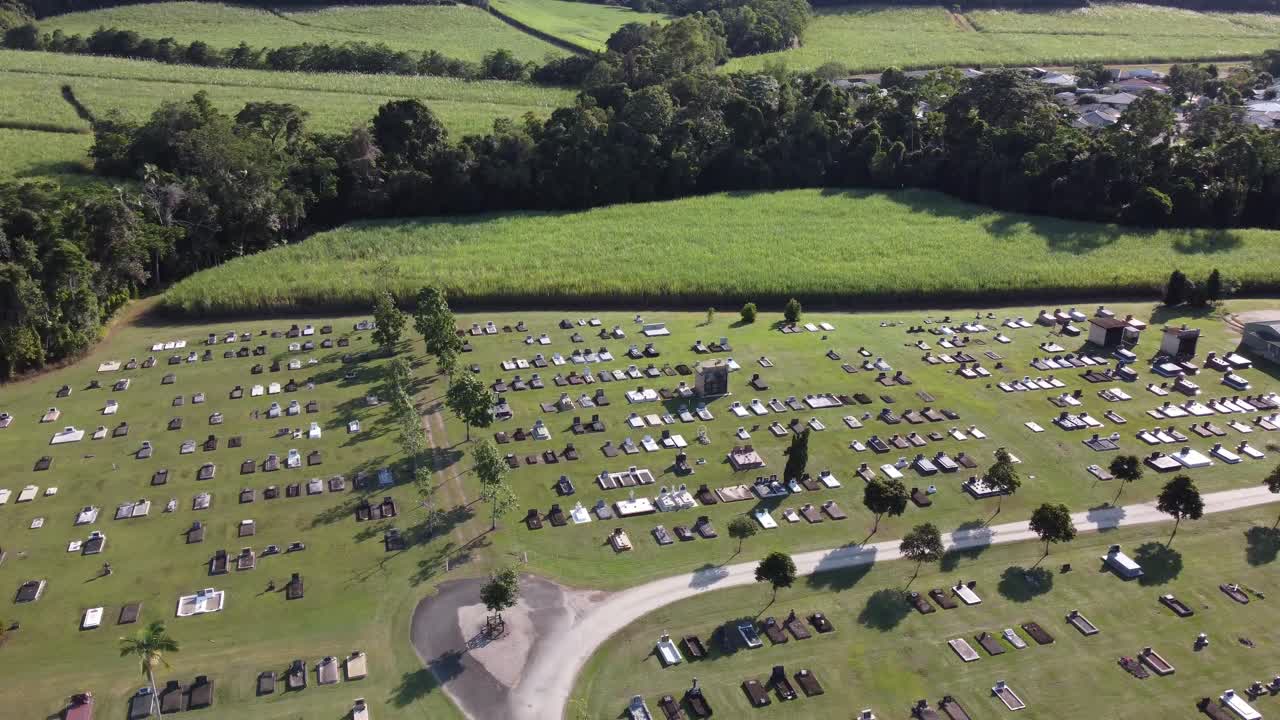 4K aerial view of a cemetery drone flying over gravestones toward the neighbouring sugarcane plantation in North Queensland, Australia