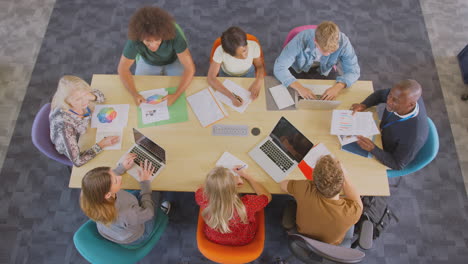 overhead shot of university or college students sitting around table with tutors in lesson