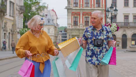 Älterer-Alter,-Stilvoller-Tourist,-Mann-Und-Frau,-Geht-Mit-Bunten-Taschen-Spazieren,-Nachdem-Er-Im-Einkaufszentrum-Auf-Der-Stadtstraße-Eingekauft-Hat