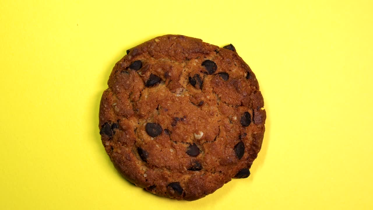 Macro de cookie com gotas de chocolate, girando lentamente em um fundo amarelo rotativo