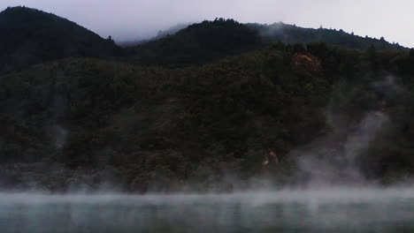 Pan-shot-of-steam-rising-over-geothermal-lake-in-active-volcanic-region-of-New-Zealand,-North-Island