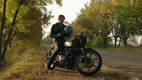 attractive man in black leather jacket comes up to his motorcycle, sits there and puts a black helmet and sunglasses before