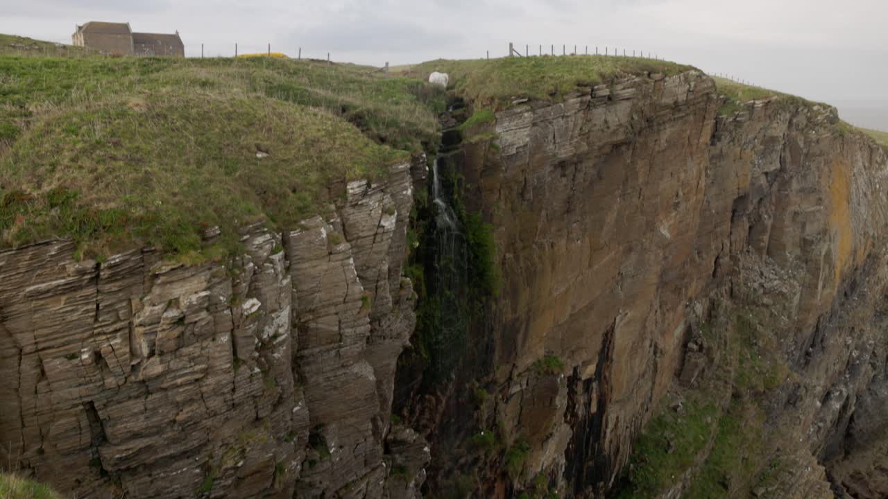 revealing shot of a small waterfall coming from the cliff at the Whaligoe Steps