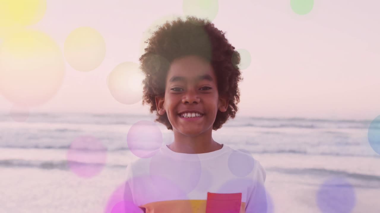 animación de puntos de luz coloridos sobre una chica afroamericana sonriente en la playa junto al mar al atardecer.