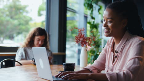 young businesswoman with coffee making video call on laptop in coffee shop