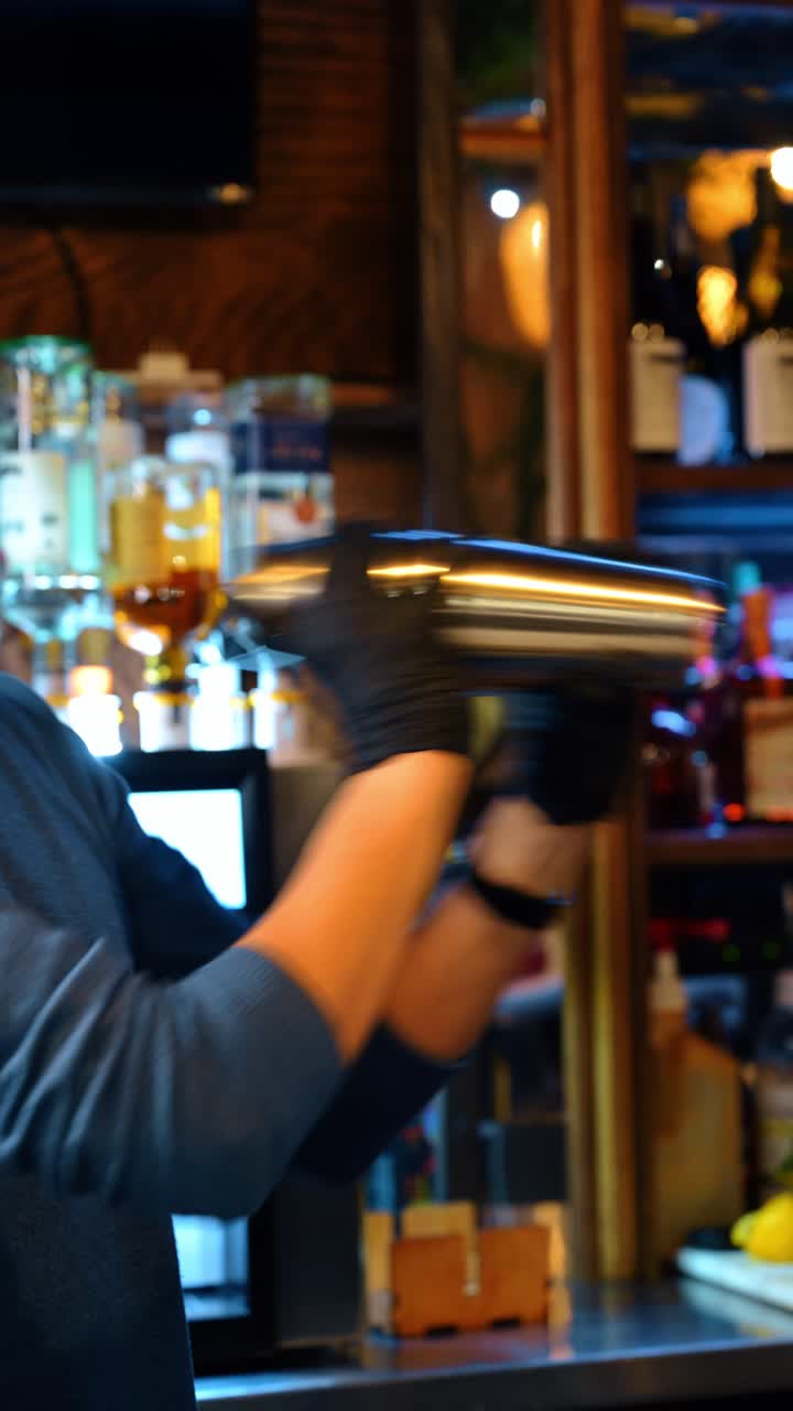 Sfocatura di movimento di un barista che agita un cocktail in uno shaker di metallo. Scatto dinamico sfocato delle mani di un barista che agita vigorosamente uno shaker d'argento in un ambiente buio di un bar.