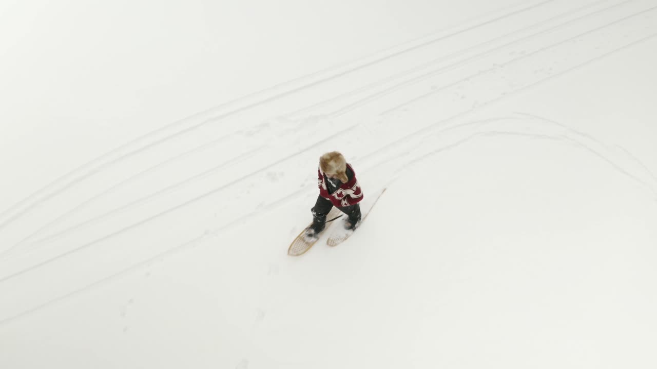 hombre adulto con un gran sombrero de piel, camina y juega con raquetas de nieve tradicionales en un lago congelado con sus perros en el norte de canadá