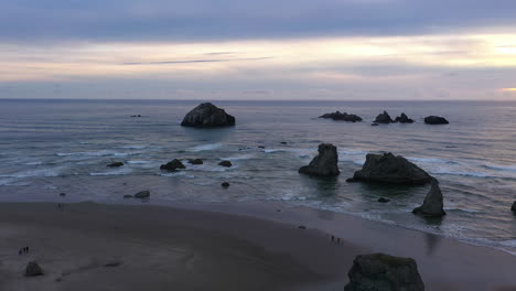 Paisaje-De-Formación-Rocosa-Con-Olas-Rompientes-Y-Visitas-Turísticas-Durante-La-Puesta-De-Sol-En-Bandon,-Oregon