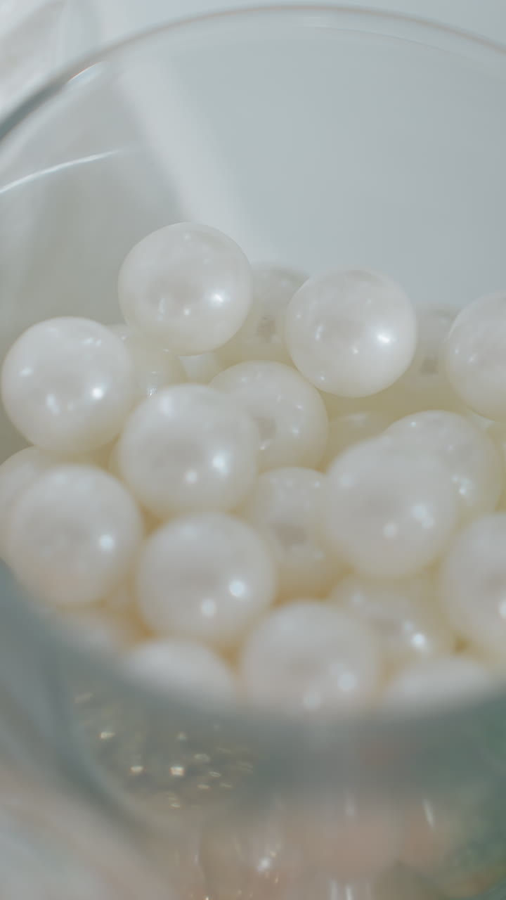 primer plano de cuentas de perlas blancas en taza de vidrio junto a cuentas decorativas de oro y verde almacenadas en pequeños frascos, cristales de azúcar en taza de vidrio, dispuestos cuidadosamente para hornear y decorar postres