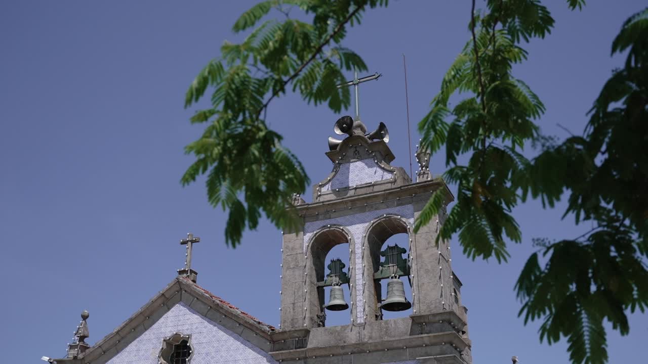 historic stone church tower with twin bells and leafy branches beneath a vibrant blue sky