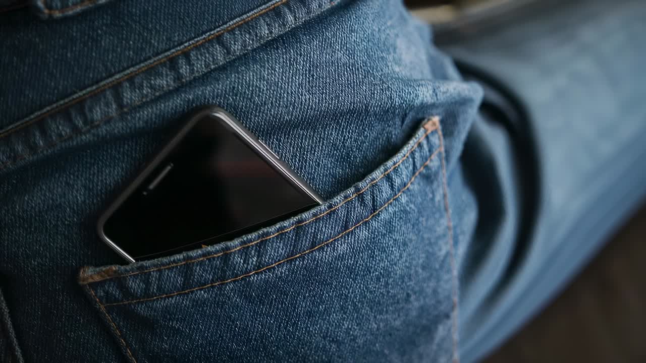 Gamba che si sposta, spingendo lo smartphone più a fondo nella tasca posteriore dei jeans di denim blu a causa del movimento da seduti