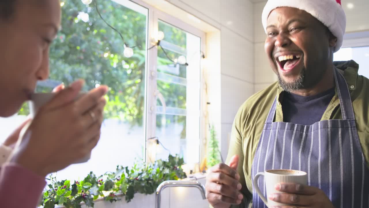 Afroamerikanska vänner som smuttar på muggar i köket, skrattar och gestikulerar efter en fråga, plats för text