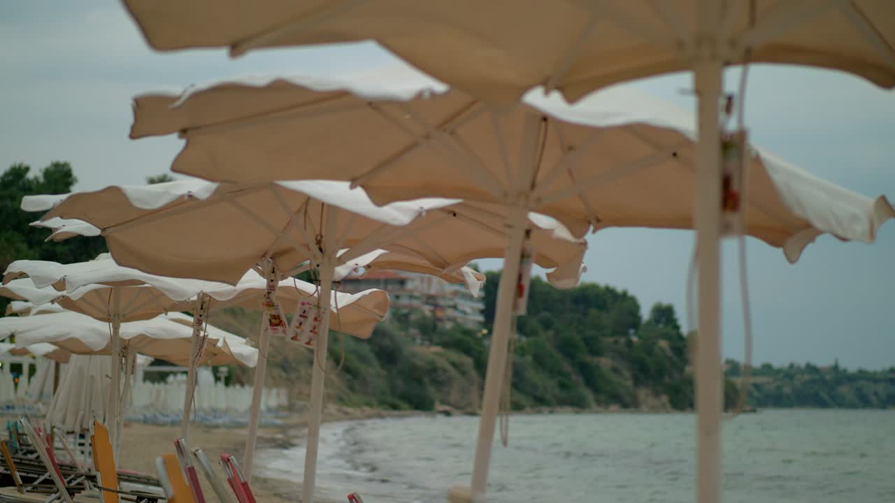 Tempo ventoso sulla riva del mare. Spiaggia deserta e ombrelloni che si muovono, Grecia.