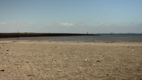 low-angle shot of a dry sand zone during low tide on the dutch coast, with a distant shoreline and soft blue sky in the background
