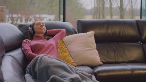 woman wearing wireless headphones listening to music streaming from mobile phone on sofa at home