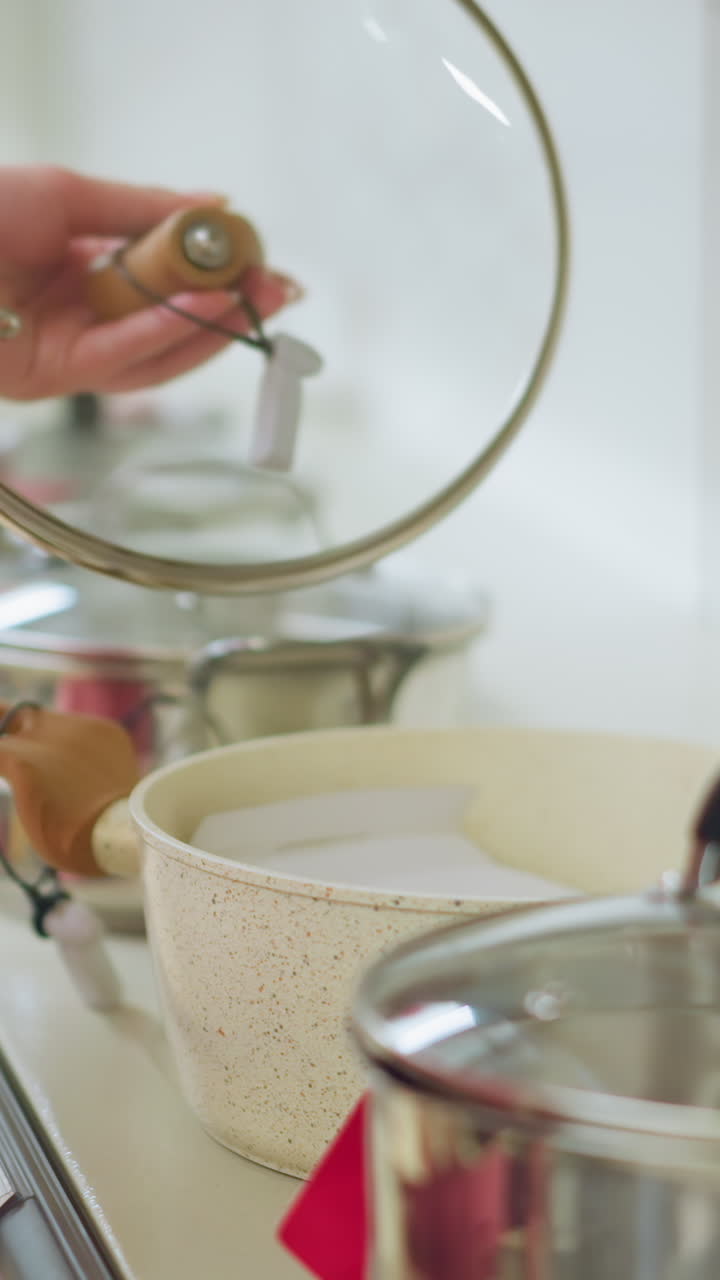 Hand of female shopper inspecting a pot in a kitchenware store, the shopper is carefully lifting the lid of a modern cookware pot with a wooden handle, surrounded by other pots on display