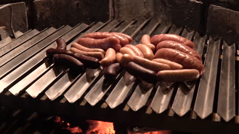 Sausages-being-fried-on-a-brick-barbecue-grill-at-night-WIDE-SHOT