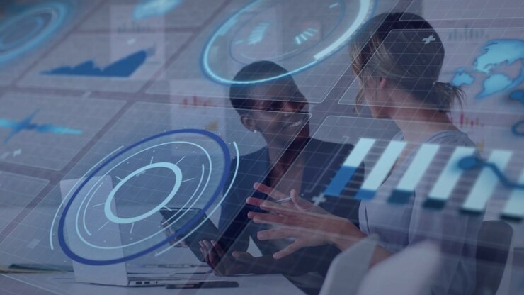 Two women reviewing tablet, right speaking gesturing, left tapping, blue HUD overlaying biz data