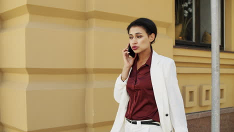 Mujer-De-Raza-Mixta-Hablando-Por-Teléfono-En-La-Calle-Urbana.-Mujer-Joven-Caminando-Al-Aire-Libre